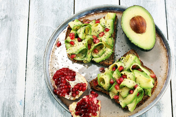 sliced avocado and ripe pomegranates on toast bread with spices and avocado.
