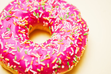 Bright donut in a pink glaze with a multi-colored rainbow sprinkle on a yellow background. 