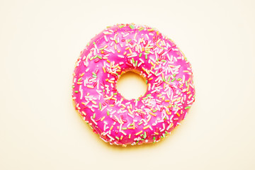 Bright donut in a pink glaze with a multi-colored rainbow sprinkle on a yellow background. 