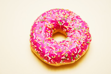 Bright donut in a pink glaze with a multi-colored rainbow sprinkle on a yellow background. 