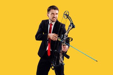 Fototapeta na wymiar Businessman aiming at target with bow and arrow, isolated on yellow studio background. The business, goal, challenge, competition, achievement concept