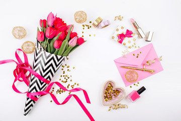 Pink and Gold Styled Desk with Florals. Pink tulips in black and white stylish wrapping paper, gifts, cosmetics and female accessories with confetti on white background