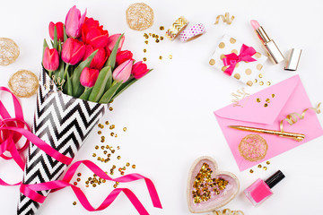 Pink and Gold Styled Desk with Florals. Pink tulips in black and white stylish wrapping paper, gifts, cosmetics and female accessories with confetti on white background