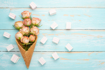 Pink roses in a cone with ice cream on a blue wooden background, concept gift for the beloved...