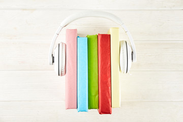 Fototapeta na wymiar Electronic audiobook vs regular paper book concept. Stack of different color hardcover books with blank colorful covers & white headphones on table. Old versus new. Close up, copy space, background.