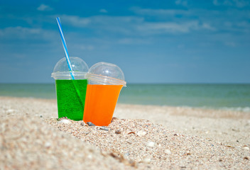 Two cocktails drink sand close-up against the background of the sea and sky,   clouds a glass a tube for drinking liquid, soda summer sun weekend rest   vacation, shore a wave of foam shells still lif