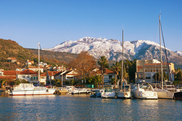 Fototapeta na wymiar Picturesque winter Mediterranean landscape. Montenegro, Bay of Kotor. View of Marina Kalimanj in Tivat city and snow-capped mountains of Lovcen