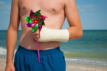 Gypsum fracture on a man's hand, toy windmill, sand close-up against the background of the sea and...