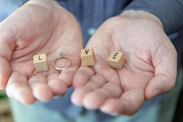 Man holding the word love in his hands made from wooden cubes anda diamond engagement ring