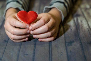 Heart in child hands. Wooden background. A child holds a heart in his hands. Valentines Day.