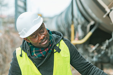 African American railroad engineer wearing safety equipment (helmet and jacket) checking gear train