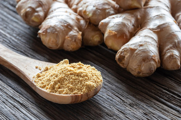 Ground ginger on a spoon with fresh ginger root in the background