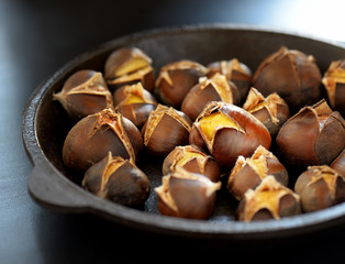 Heap of grilled edible chestnuts in cast iron skillet over dark wooden surface