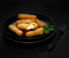 Delicious breaded mozzarella cheese sticks on a black plate on a dark background
