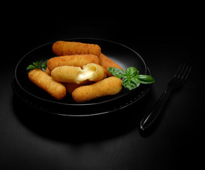 Delicious breaded mozzarella cheese sticks on a black plate on a dark background
