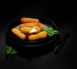 Delicious breaded mozzarella cheese sticks on a black plate on a dark background