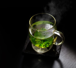 hot mint tea in a glass mug on a dark background