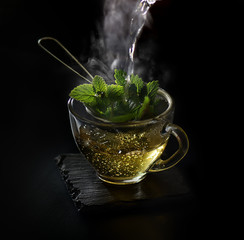Pouring mint tea from the kettle into a glass cup on a dark background