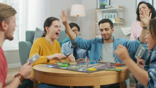 Diverse Group of Guys and Girls Playing in a Strategic Board Game with Cards and Dice. Cozy Living Room in a Daytime