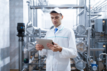 man in a white robe with a tablet in his hands is in the production shop at the factory
