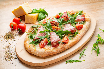 Flatbread pizza garnished with fresh arugula on wooden pizza board