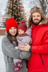 young energetic family. Husband and wife hug their child on the street in the middle of a snow-covered winter in a park near a tree. Enjoying spending time together. Family concept.