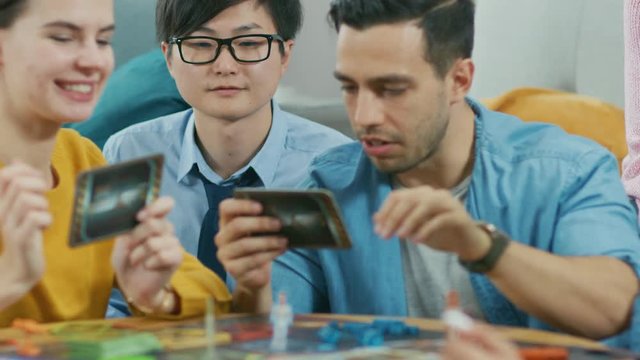 Diverse Group of Guys and Girls Playing in a Strategic Uniquely Designed Board Game with Cards and Dice. Friends Having Fun Reading Cards, Joking, Making Moves and Laughing in a Cozy Living Room
