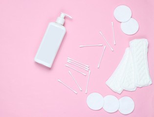 Hygiene products on a pink pastel background. Cotton pads, women's pads, bottle of cream, cotton ear sticks. Top view, flat lay, copy space.