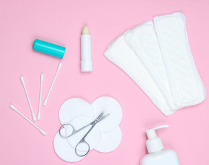 Products for hygiene, skin care and nail manicure. Cotton pads, cotton buds, nail scissors, bottle of cream, feminine pads on pink background. Top view, flat lay.