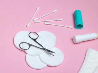 Products for hygiene, skin care and nail manicure. Cotton pads, cotton buds, nail scissors, bottle of cream, feminine pads on pink background..