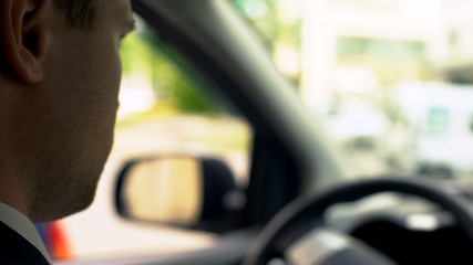 Young businessman driving car in city traffic, going to office meeting, close up