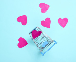 Mini shopping trolley, decorative hearts on blue background, top view, minimalism. Conceptual...