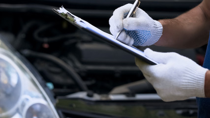 Mechanic diagnoses car, writing costings, annual vehicle inspection, close up