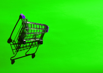 Mini shopping trolley for shopping on green background, consumer concept, minimalism, top view, hard light, shadow.