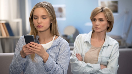 Daughter with smartphone in hands ignoring mom, misunderstanding and conflict