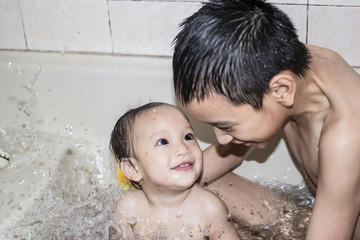 Little child in a bathtub, Happy baby taking a bath playing with older brother.