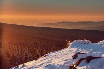 Mountain view down to the valley and forest with snow in the foreground and colorful orange tones from sunset. Harz Mountains National Park in Germany