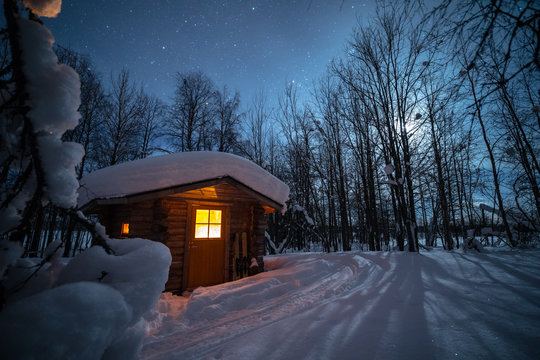 Illuminated log cabin in forest at night during winter