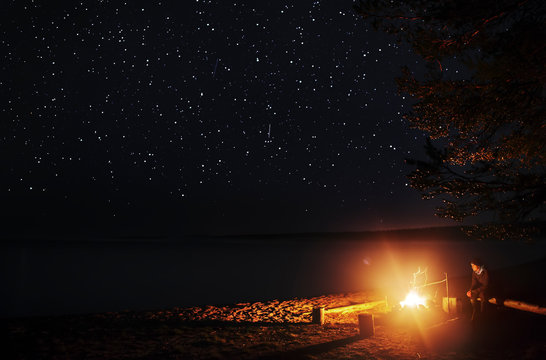 Man sitting on wooden log near campfire at night