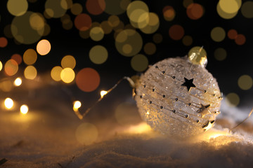 Christmas ball and glowing lights on snow against blurred background, space for text. Winter decor