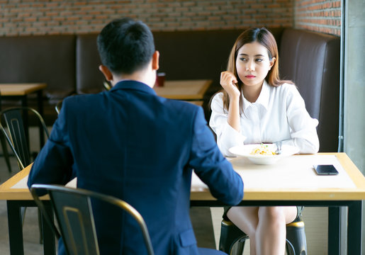 Tired Bored Asian Girl Sitting And Lunch With Her Boyfriend At A Cafe  And Looking Away.Young Emotional Couple Get Quarreled In Cafe.