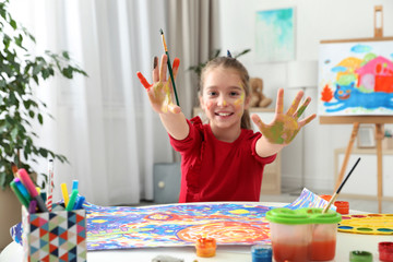 Naklejka premium Little child with painted hands and face at table indoors