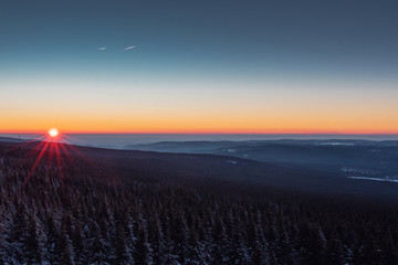 Mountain winter landscape with snow and pine forest. Colorful sunset view from the top of the mountains with valley fog in the evening. Wolfswarte, Torfhaus, Harz Mountains National Park in Germany