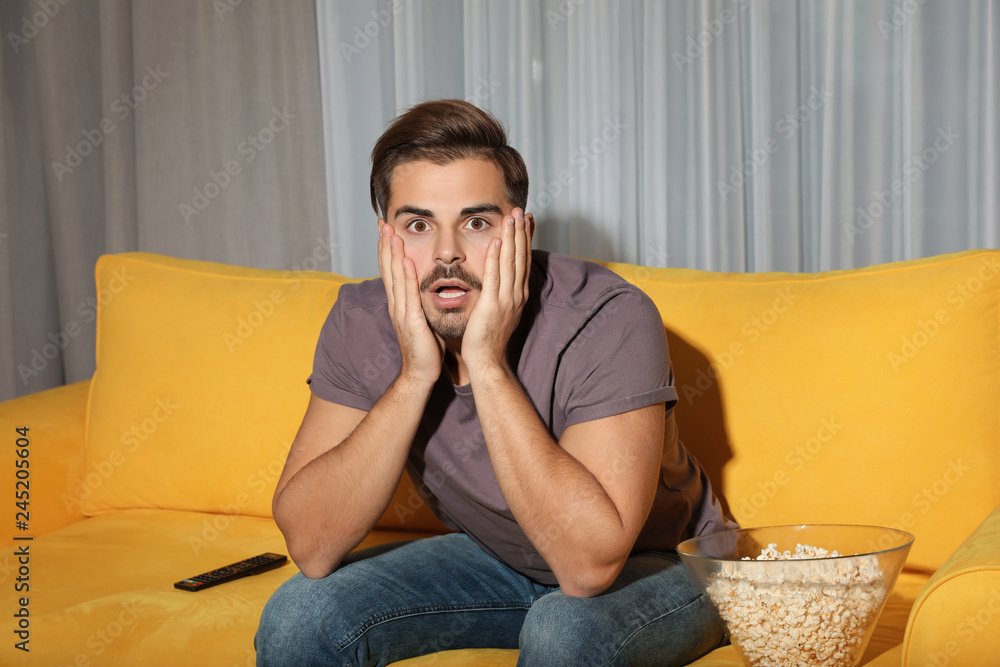 Poster emotional man watching with popcorn tv on couch in living room