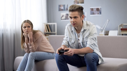 Unhappy girl looking at her boyfriend who indifferently playing video games