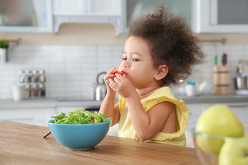Cute African-American girl eating vegetable salad at table in kitchen © New Africa
