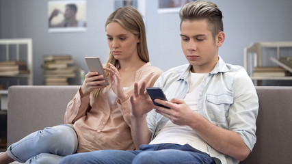Couple in love indifferently sitting on couch looking at their smartphones
