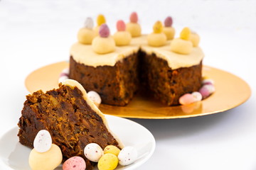 Fototapeta na wymiar Easter Simnel Cake. Simnel cake with marzipan topping and eleven balls of marzipan representing the twelve apostles minus Judas. Mini chocolate Easter Eggs round the base. Focus on the slice.