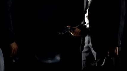 Obraz na płótnie Canvas Illegal weapon trafficking, man in suit checking handgun holding bag with money