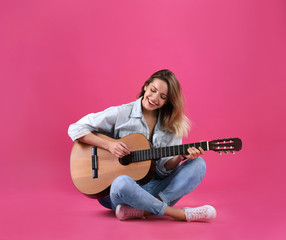 Young woman playing acoustic guitar on color background